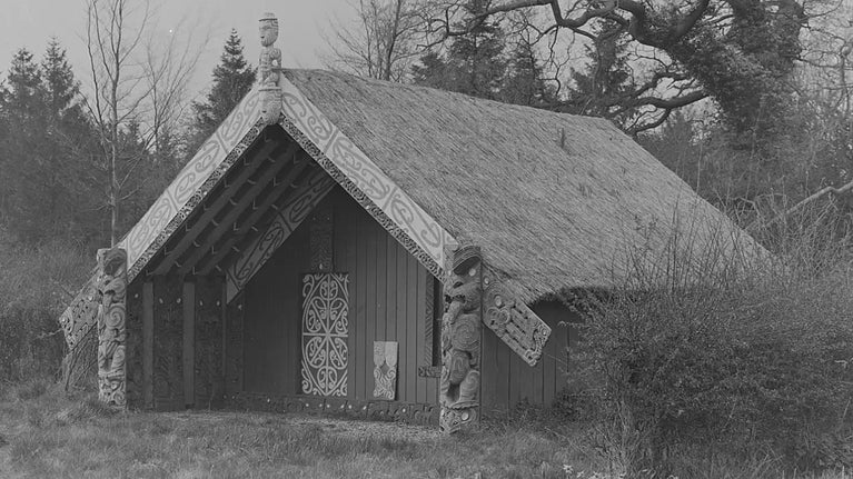 A black and white image of a gabled Maori meeting house with a thatched roof